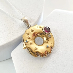 Macro shot of 18k gold donut pendant with colorful zircons on white platform