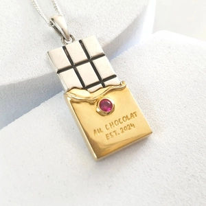 Macro detail of silver chocolate bar pendant with red gemstone on 18k gold foil