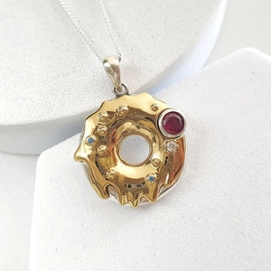Macro detail of donut pendant with gold icing, red gemstone, and zircon inlays on silver chain