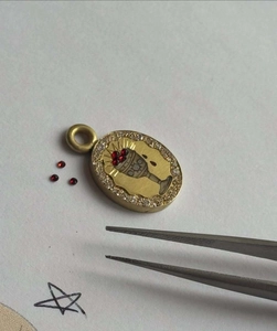 Macro shot of oval gold pendant with chalice engraving, red gemstones and zircon halo