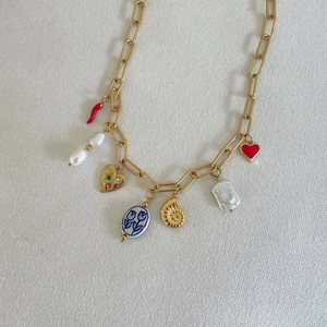 Detailweergave van gouden paperclip ketting met kleurrijke bedeltjes op crèmekleurige stof