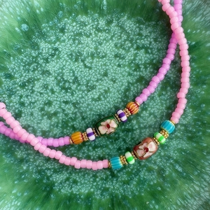 Detalle de collar de cuentas coloridas con flores rosas y ojo turco en bandeja verde