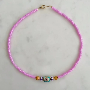 Detalle de collar de cuentas coloridas con dije de flor esmaltada azul y cuentas púrpuras