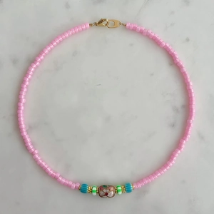 Detalle del collar de cuentas rosas con flores de colores, dijes de ojo y un cierre dorado
