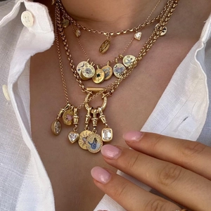 Detail of layered gold titanium necklaces with painted charms and heart crystal on white linen