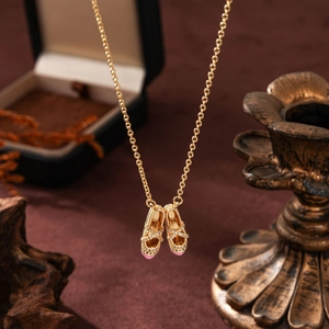Detailed close-up of a golden ballet shoe necklace pendant with pink enamel and crystals