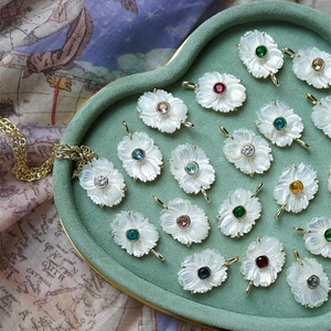 Vue détaillée de pendentifs fleurs en nacre avec pierres précieuses colorées dans un écrin