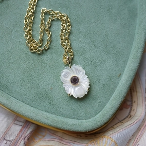 Détail du collier avec pendentif fleur en nacre et pierre violette sur un support velours vert