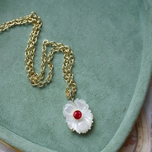 Gros plan d'un pendentif marguerite blanche avec zircon rouge sur une chaîne à maillons dorés