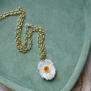 Détail du collier doré avec pendentif fleur blanche et pierre de zircon jaune centrale