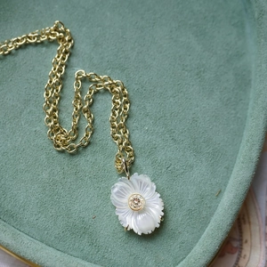 Vue macro détaillée du pendentif fleur en nacre blanche sur une chaîne à maillons dorés