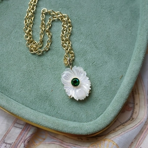 Détail du collier fleur avec pétales en nacre et pierre verte sur un plateau chic