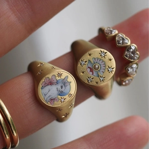 Detailed close-up of 18K gold signet rings with rabbit painting and heart gemstones