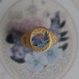 Macro view of gold signet ring featuring floral enamel, inset diamonds, and star engravings