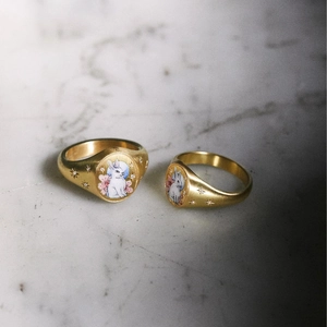 Detail of gold signet rings with rabbit and floral motifs on marble surface