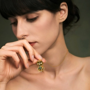 Collar de relicario dorado vintage con trébol verde usado por modelo sobre fondo verde