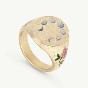 Macro detail of gold signet ring with moon phases engraving and pink rose enamel pattern