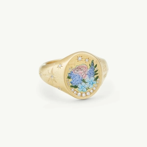 Close-up of golden signet ring featuring pink rose enamel and star-set crystal details