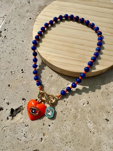 Détail du collier perlé avec pendentif cœur orange et œil protecteur sur plateau