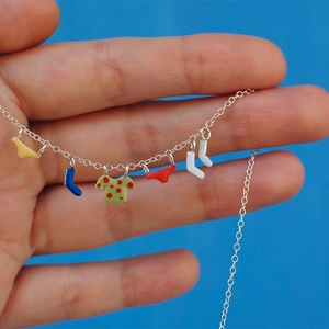 Detail of colorful enamel clothing charms on a silver necklace held by hand