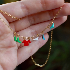 Detail shot of a gold necklace with colorful enamel laundry-shaped charms on a hand