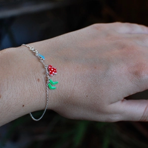 Detail of a minimalist silver chain bracelet with colorful enamel charms on wrist