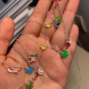 Detail of silver necklace featuring colorful enamel shirt and sock charms on hand