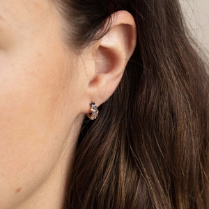 Nahaufnahme von goldenen Ohrsteckern mit blauen und weißen Zirkonia, getragen von einem Modell