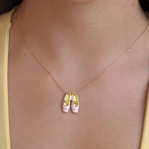 Elegant close-up of pink ballet slippers pendant on a gold necklace worn by a model