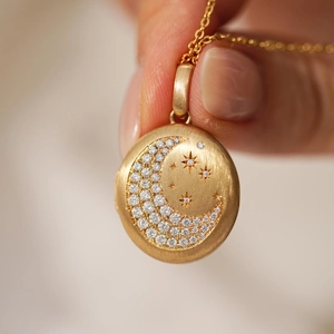 Detalle del relicario dorado con incrustaciones de circón luna y estrella, acabado mate
