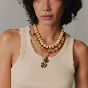 Detail van een drielaagse kralenketting met gouden hangers op een beige vest