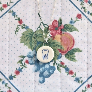 Dettaglio della collana con pendente tondo argento e dente su sfondo floreale