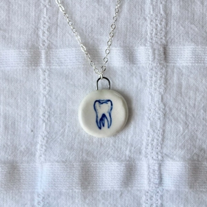 Dettaglio del ciondolo rotondo in ceramica con dente blu su sfondo di tessuto a nido d'ape