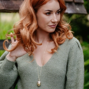 Elegante collana con medaglione a ghianda dorata indossata da una modella su sfondo verde