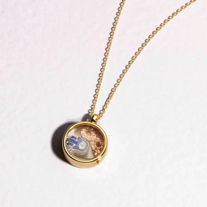 Close-up of golden floating locket with blue Hamsa hand charm and orange crystal