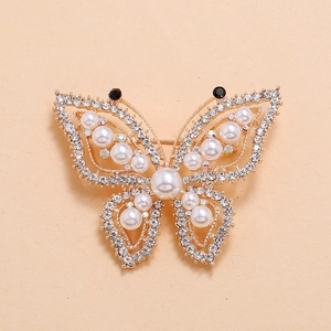 Elegant gold butterfly brooch with shimmering rhinestones and white pearls on yellow background