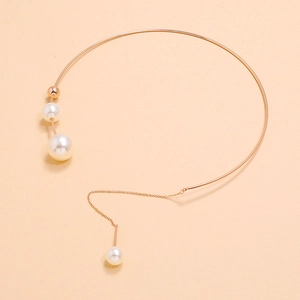 Detailed macro view of gold choker necklace featuring polished pearls and dangling chain detail