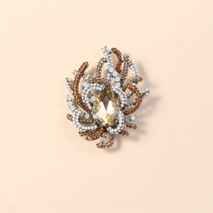 Elegant drop-shaped crystal brooch with amber rhinestones on a beige background