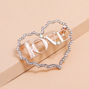 Broche cœur dorée avec lettres LOVE et strass posée sur un fond aux tons chauds