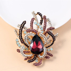 Detail of vintage gold brooch featuring a large teardrop purple gemstone and colorful rhinestones
