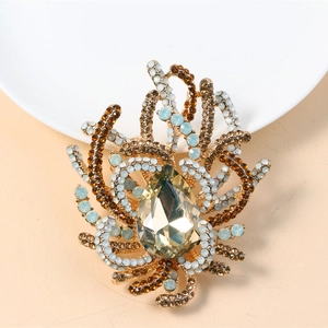 Macro detail of ornate gold brooch with water-drop crystal and coral-like branch design