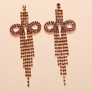 Macro detail of long gold tassel earrings with dark red rhinestones for evening wear