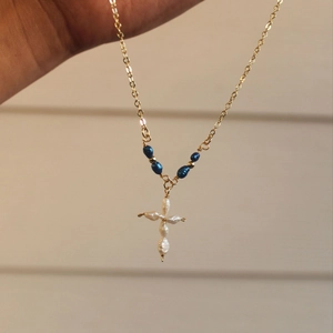 Gedetailleerd beeld van een gouden roestvrijstalen ketting met parelkruis en blauwe kralen