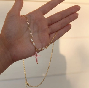 Detail van goudkleurige ketting met witte parels en roze kralen kruisvormige hanger