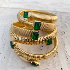 Macro view of four 18K gold-plated Tubogas bracelets with emerald-cut green gemstones
