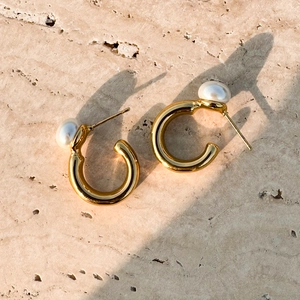 Gros plan de boucles d'oreilles dorées en C avec perle blanche sur surface en pierre