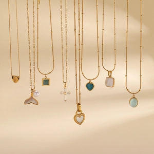 Close-up of assorted gold plated necklaces with pearl and zircon charms on a beige backdrop