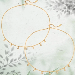 Elegante collana a due strati dorata con pendenti in zircone su sfondo di foglie