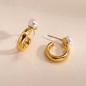 Élégantes boucles d'oreilles en C dorées avec une perle ronde blanche sur fond beige