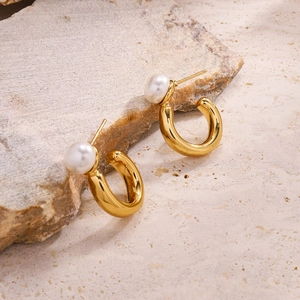 Boucles d'oreilles créoles C dorées avec perles présentées sur un socle en pierre naturelle